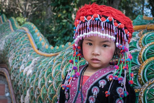 A young girl wearing traditional Thai attire with vibrant headdress enjoying a festival outdoors.