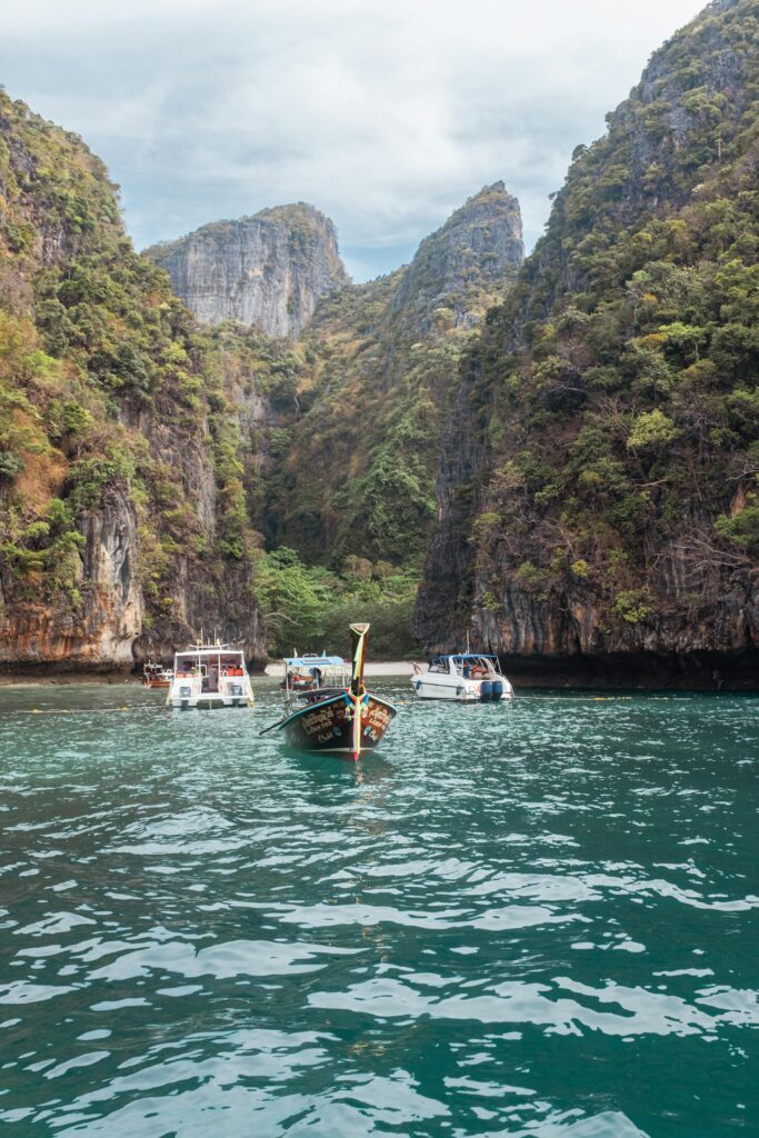 Long-tail boats exploring a picturesque limestone cliff cove under a clear sky, capturing nature's beauty.